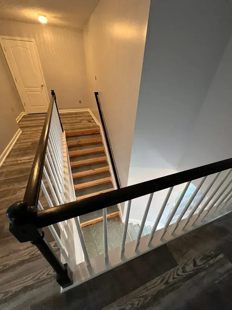 Stairwell with wooden stairs and black railings in a beige hallway, viewed from the top landing