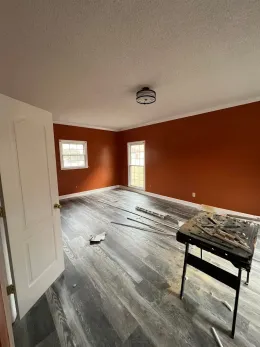 Empty room being renovated with orange walls, white trim, and dark floors under a ceiling light.
