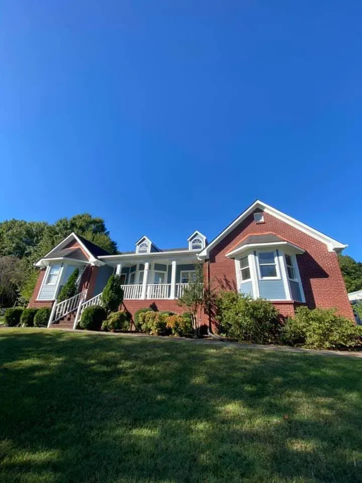 Brick suburban house with white trim and a front porch on a sunny green lawn under a clear blue sky