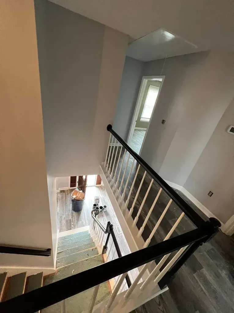 Stairwell with black railing, white walls, and a tall window letting in daylight.