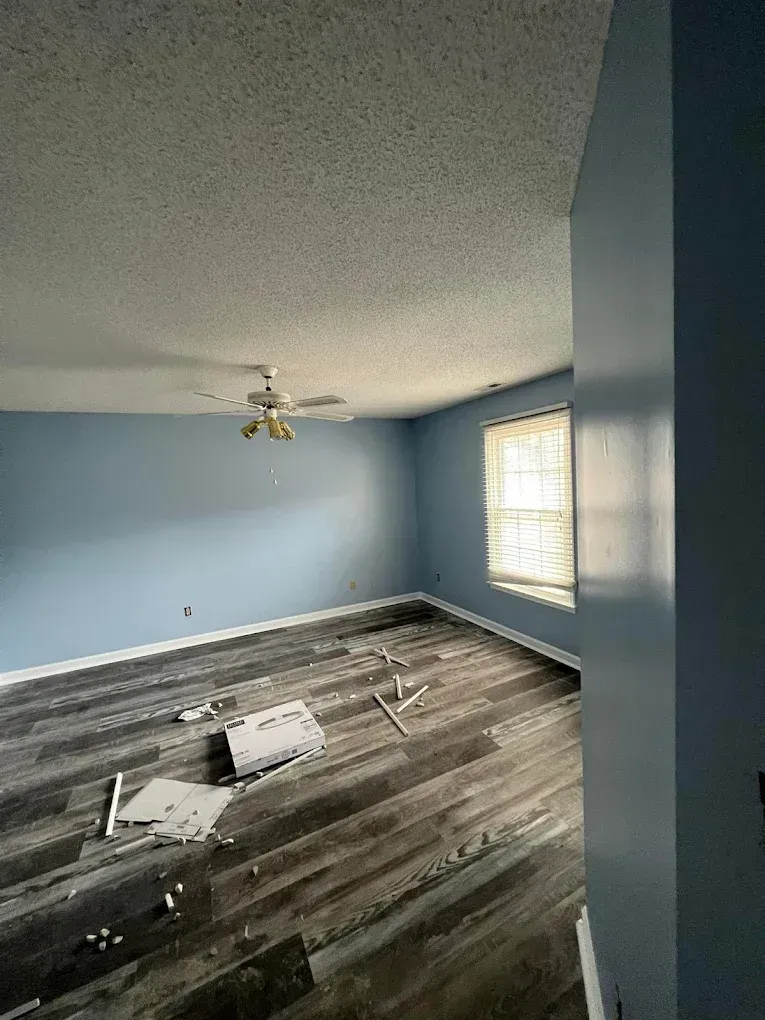 Empty blue room with patterned carpet being removed, ceiling fan, and sunlight through a window
