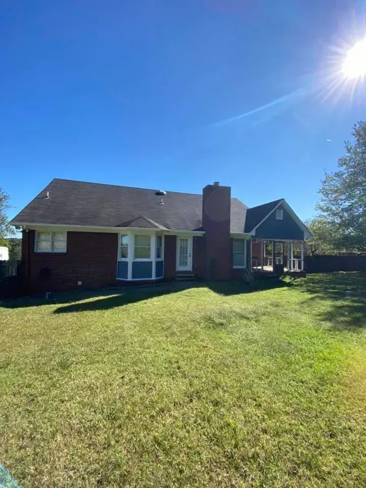 Brick house with chimney and blue siding on a sunny lawn under a clear sky