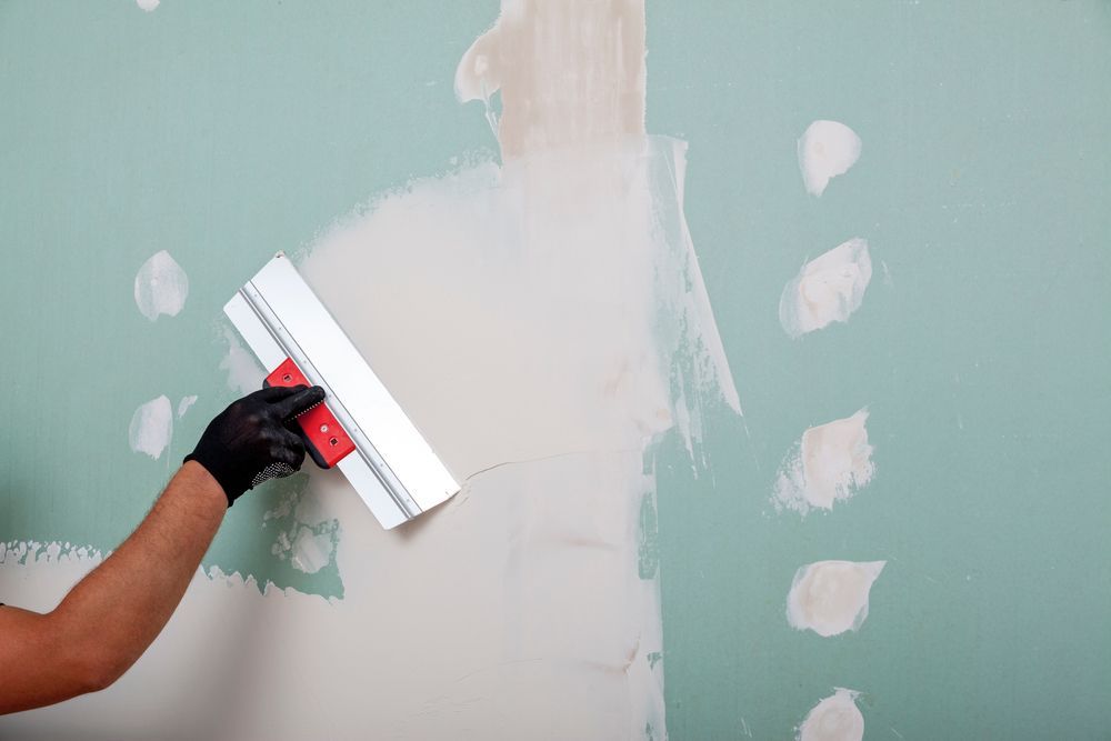 Hand sanding patchy green and white wall with a squeegee-like tool