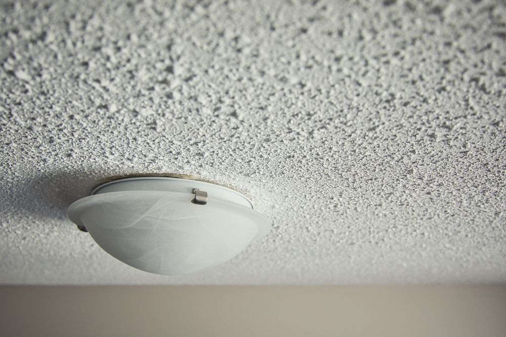 White ceiling light fixture on a textured ceiling with a small exposed wire.