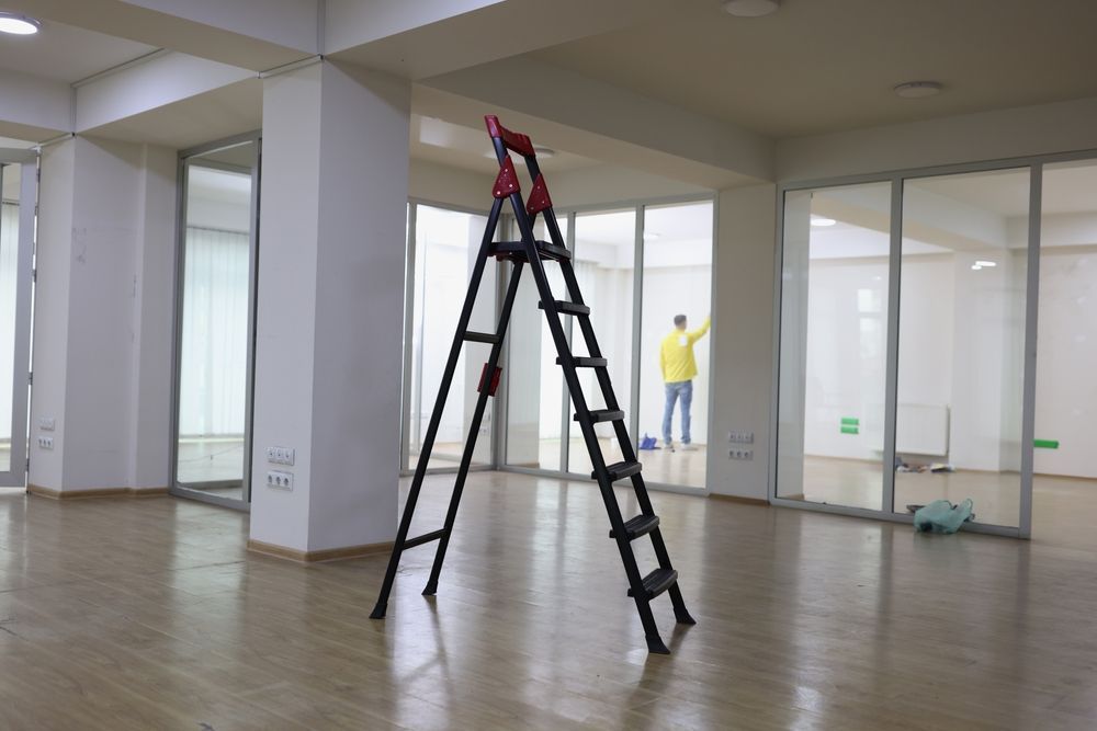 Empty office with two ladders and a person in a yellow shirt in the background