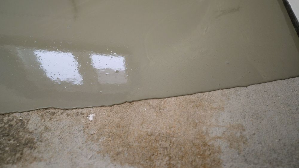 Glossy greenish surface above a rough, stained beige wall or floor edge