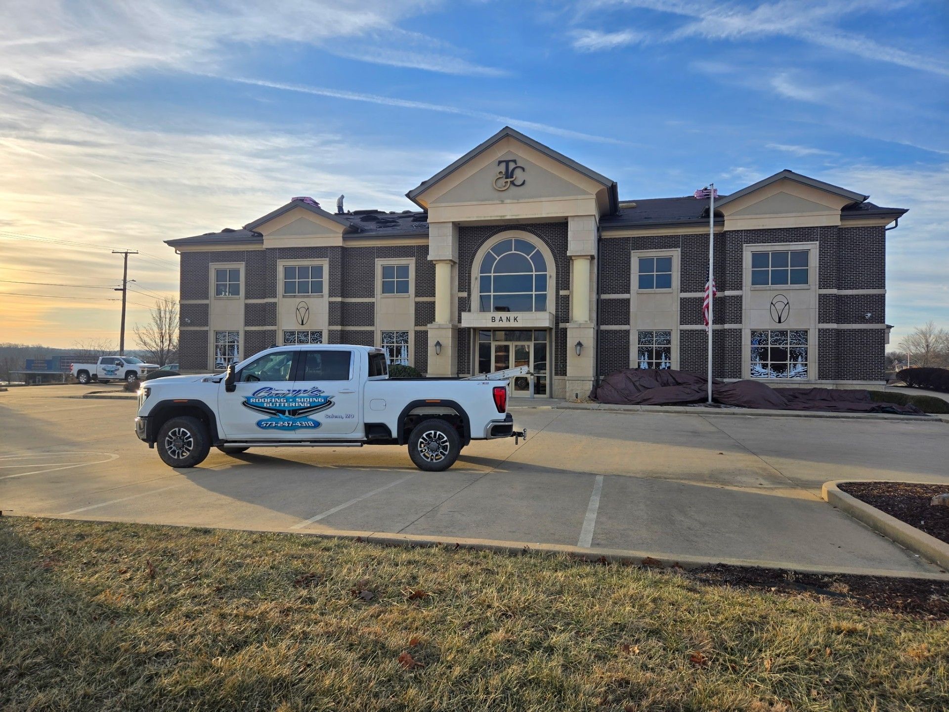 White pickup truck with logo parked in front of a large brick building at sunset