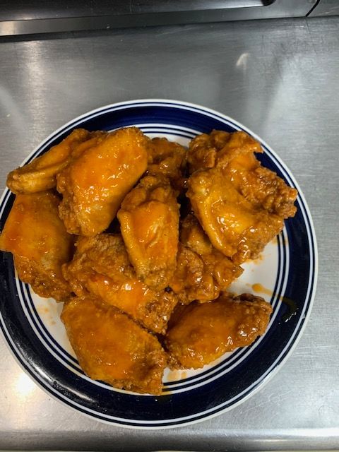 A plate of golden-orange buffalo chicken wings on a round white plate with blue rings, resting on a metal surface.