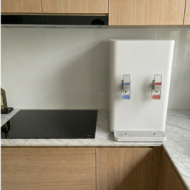 Kitchen counter with a white water dispenser and two taps, next to a black appliance mat.