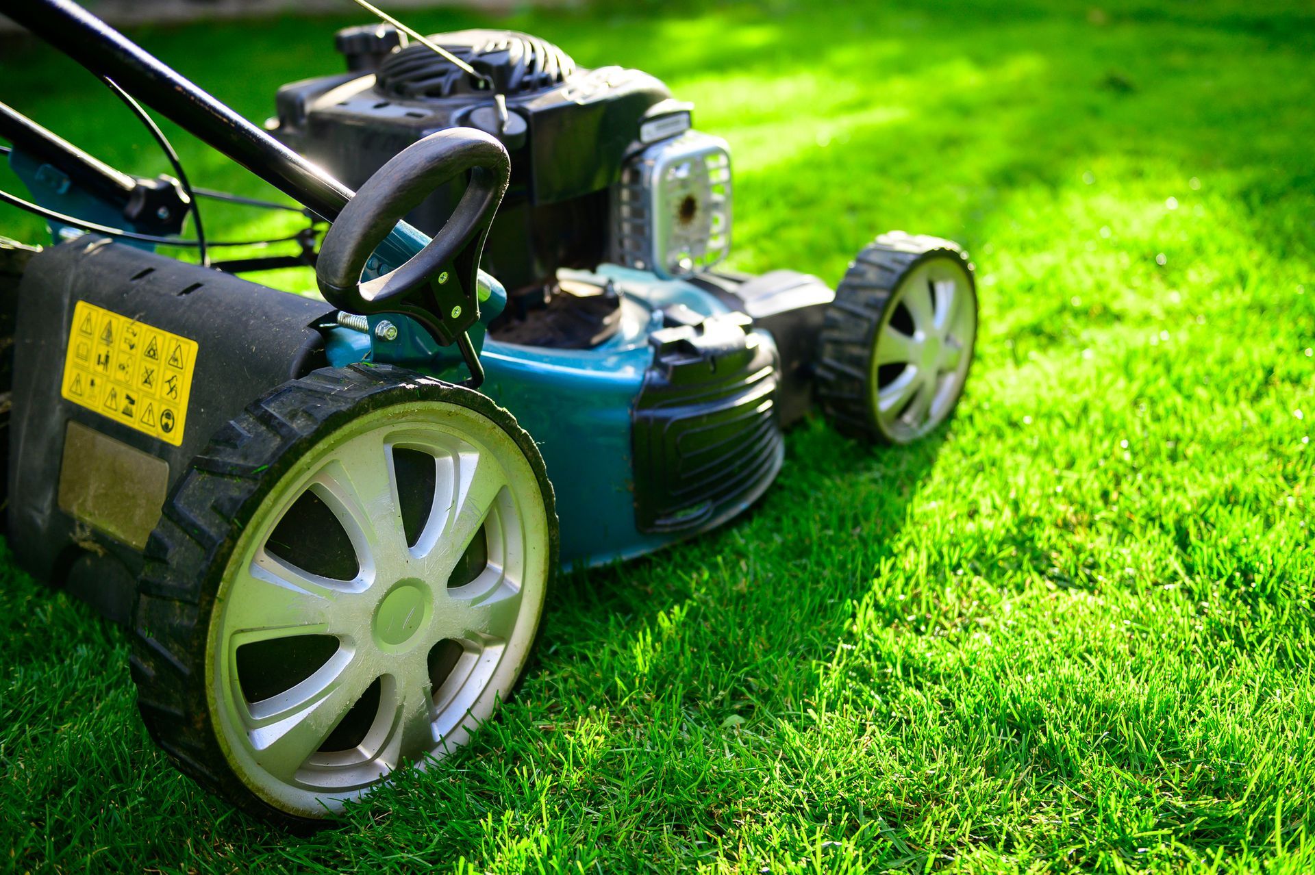 A lawn mower close-up on fresh grass, showing the wheel and engine under bright sunlight