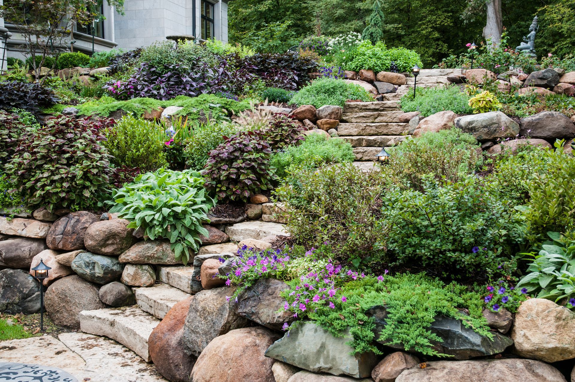 Terraced rock garden with stone steps, green shrubs, and purple flowers on a hillside
