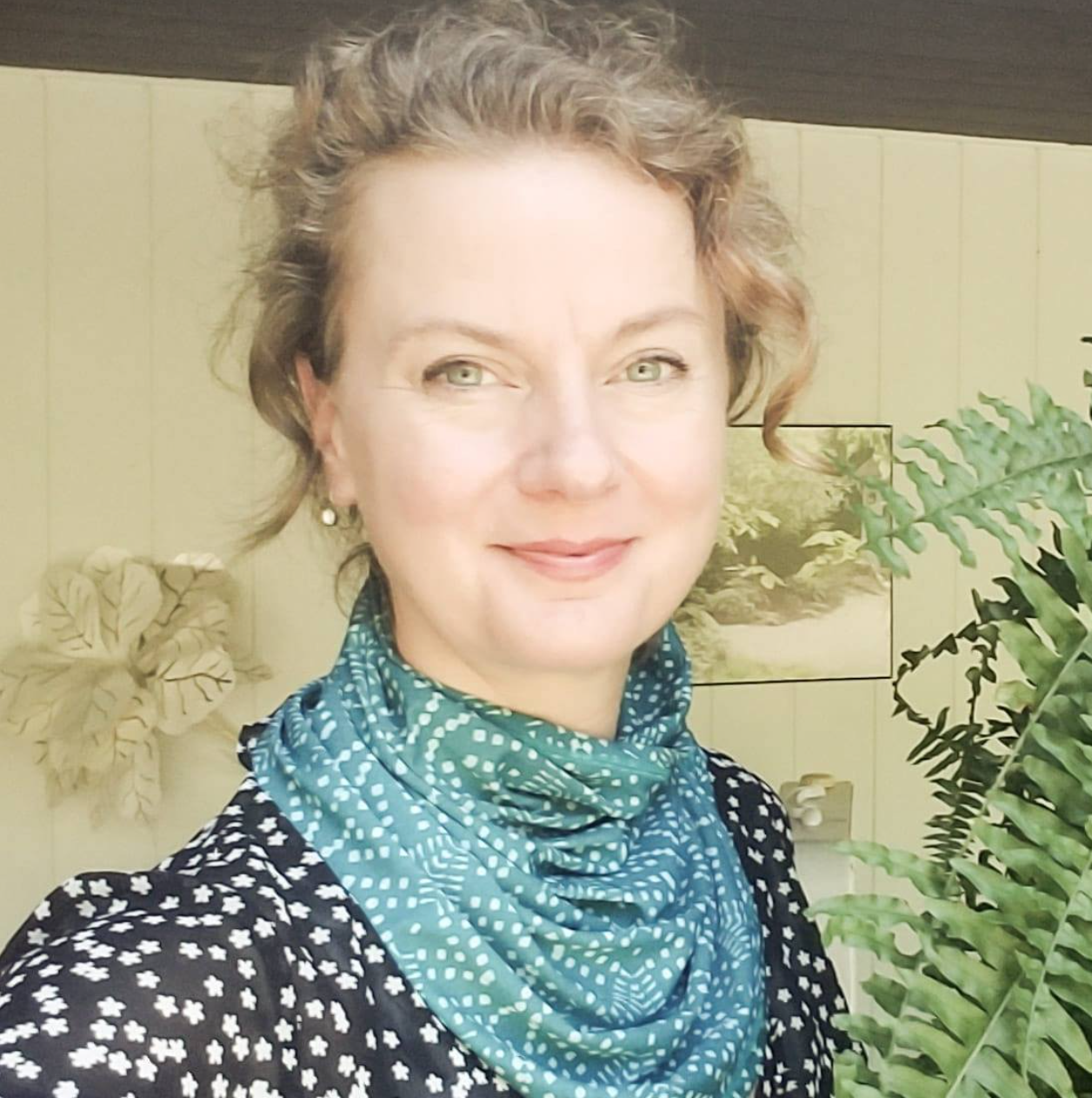 Portrait of a smiling person in a teal scarf beside green fern leaves outdoors