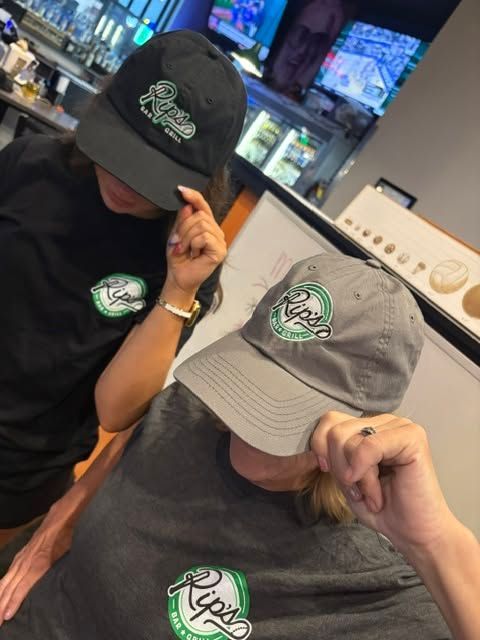 Two people in black and gray caps and shirts with a green logo, looking down in a store.