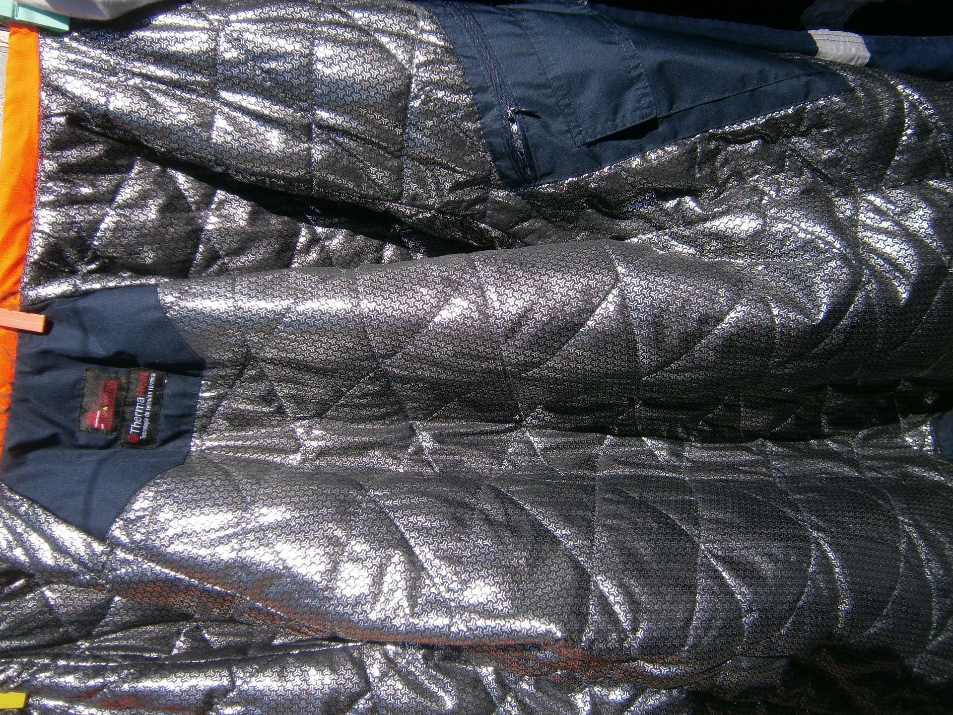 Interior de una chaqueta azul oscuro con forro térmico reflectante acolchado de color plateado.