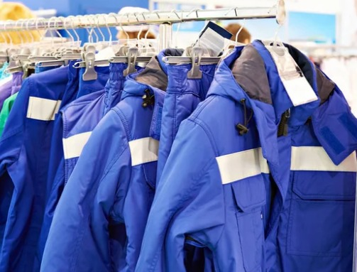 Varias chaquetas de trabajo azules con tiras reflectantes de seguridad colgadas en un perchero.