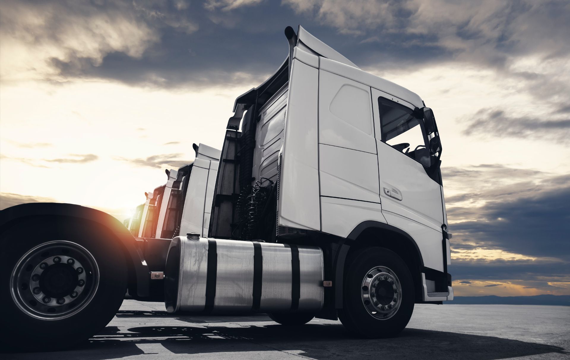 White semi-truck parked with sunset sky background.
