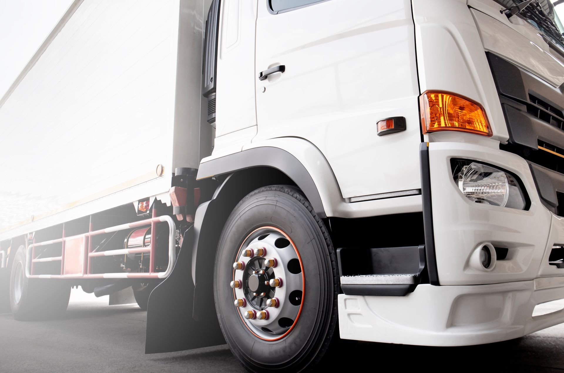 White semi-truck with orange blinker and black tire on asphalt.