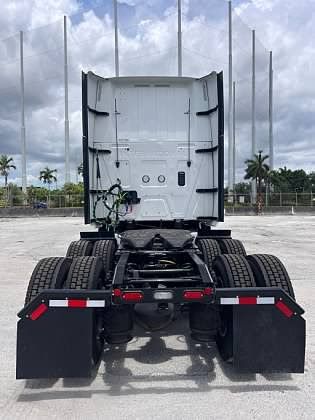 Rear view of a white semi-truck with black mud flaps and a trailer hitch, parked outside.