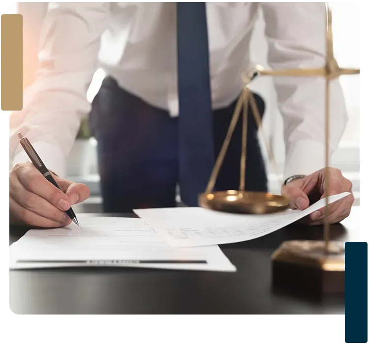 A man is writing on a piece of paper in front of a scale of justice.