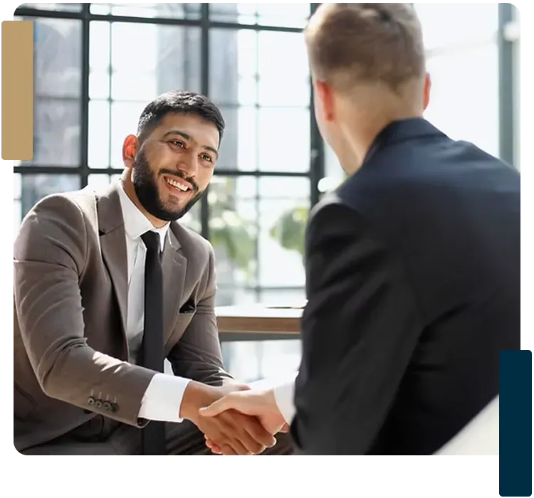 Two men in suits are shaking hands while sitting at a table.