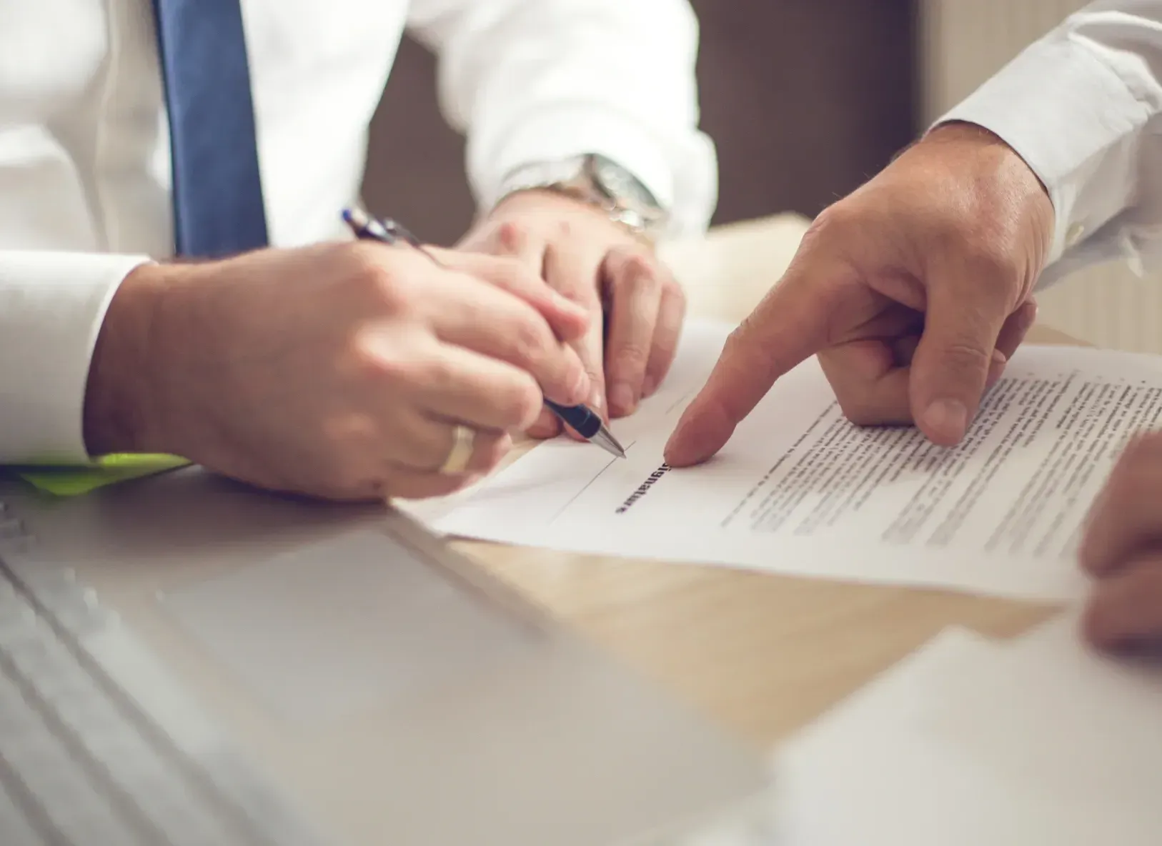 Two men are sitting at a table signing a document.