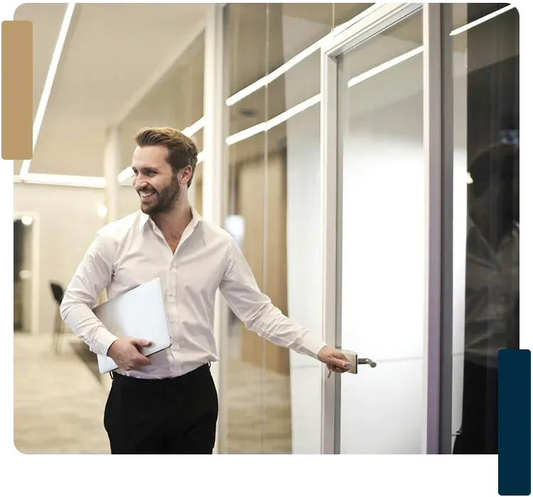 A man is holding a laptop and walking through a doorway.