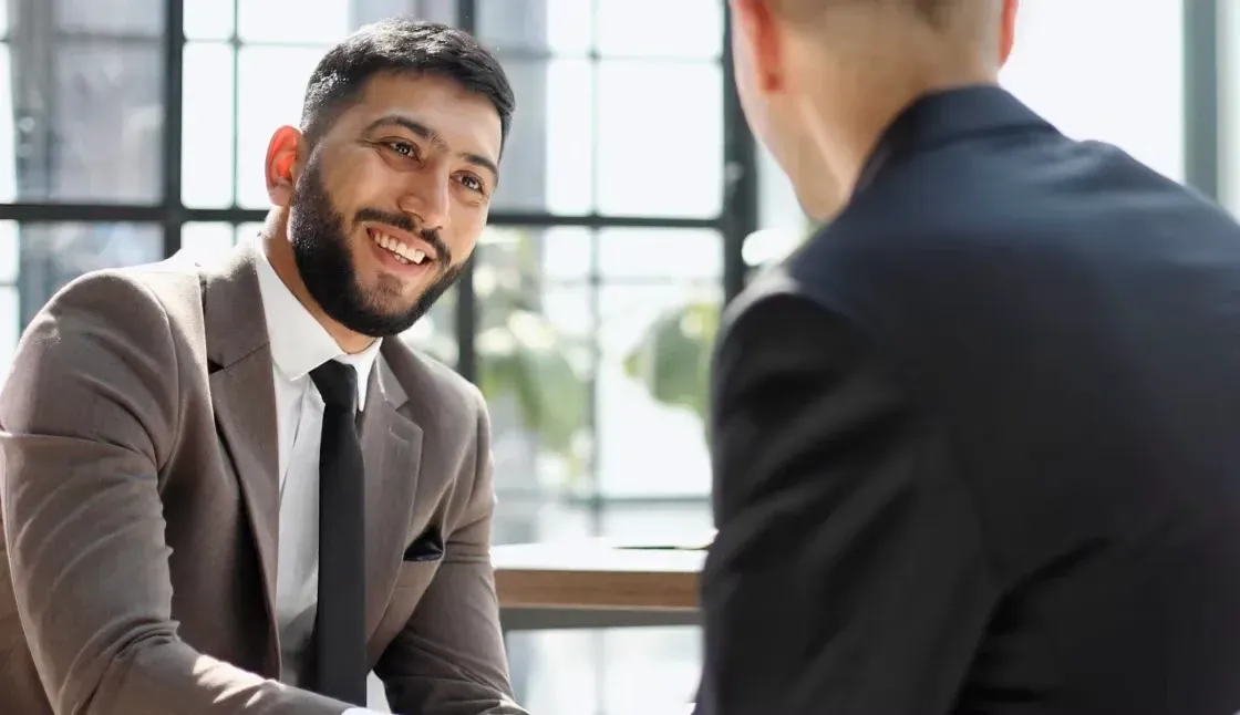Two men in suits and ties are sitting at a table having a conversation.