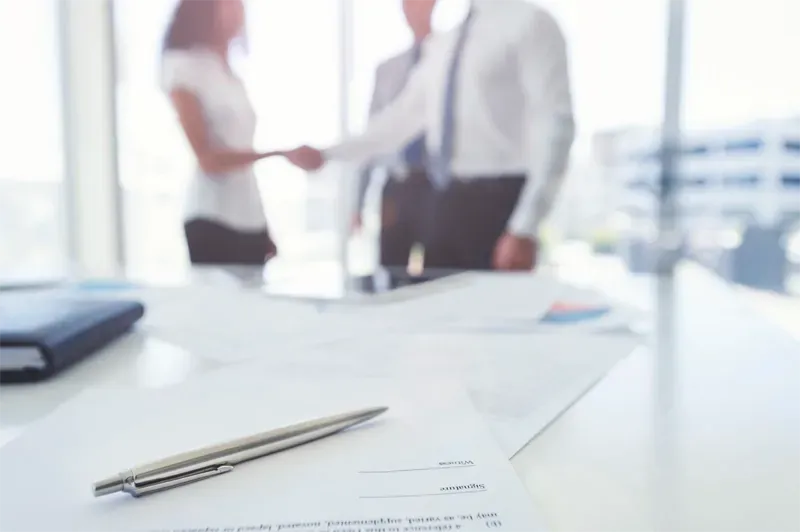 A pen is sitting on a table in front of a group of people shaking hands.