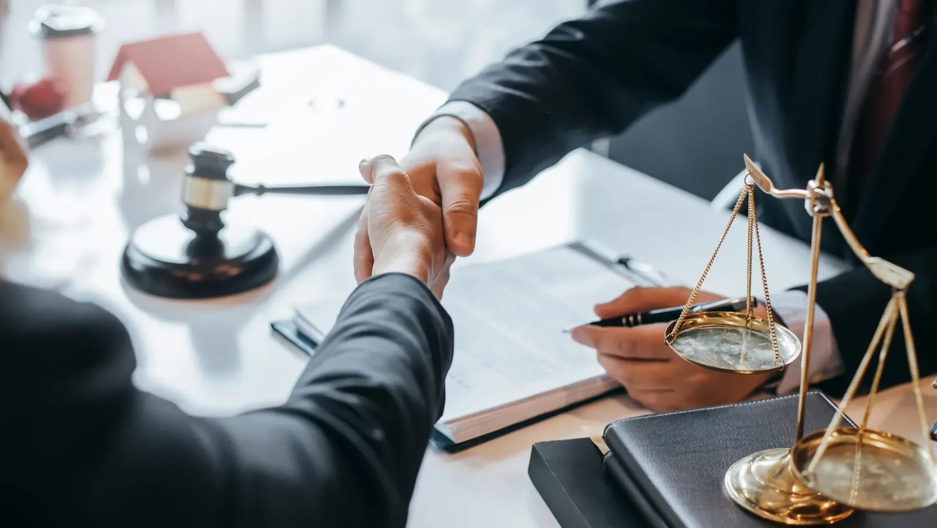 A lawyer is shaking hands with a client while holding a scale of justice.