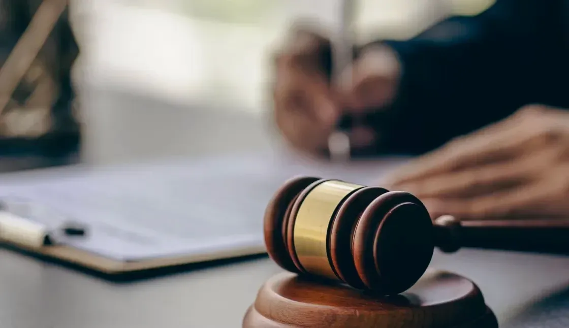 A judge 's gavel is sitting on a table next to a person writing on a clipboard.