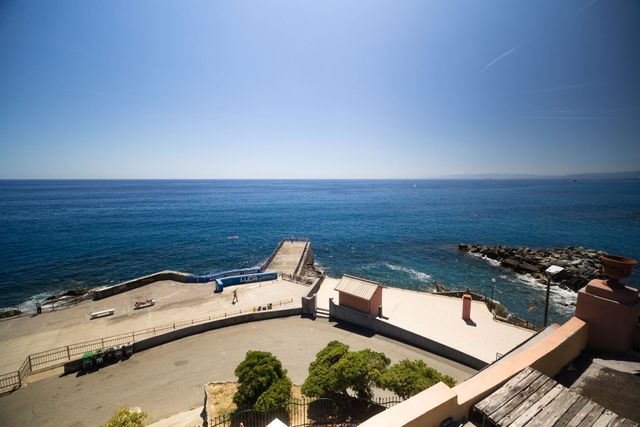 Terrazza fronte oceano con pontile che si estende in un mare blu e calmo sotto un cielo limpido.