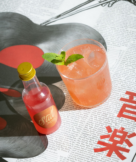 Cocktail rosa e bottiglia rossa su una pagina di rivista con testo giapponese e illustrazione grafica nera.