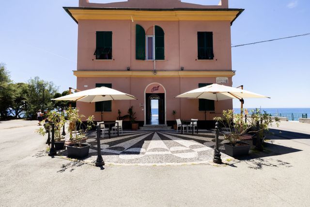 Caffè rosa a due piani sul lungomare, con ombrelloni e tavolini all'aperto.