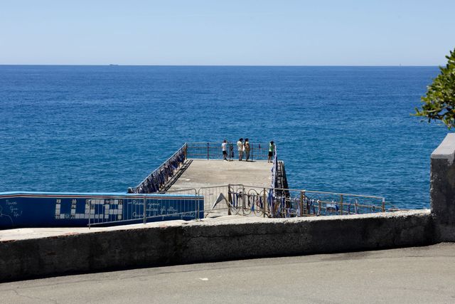 Un molo in pietra che si protende nell'oceano blu, con alcune persone in piedi all'estremità.