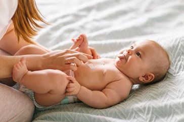 Baby lying on a bed, smiling and holding an adult’s fingers