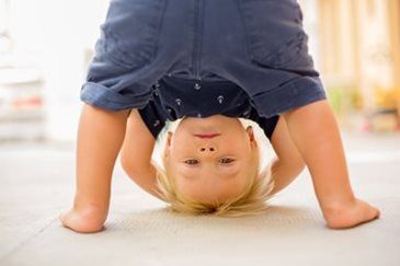 Toddler doing a handstand indoors on a light-colored floor, wearing a dark blue outfit.