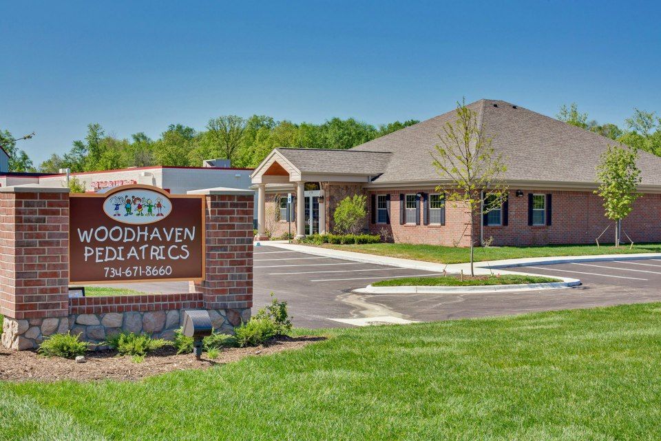 Woodhaven Pediatrics building with brick sign, driveway, and green lawn under a clear sky