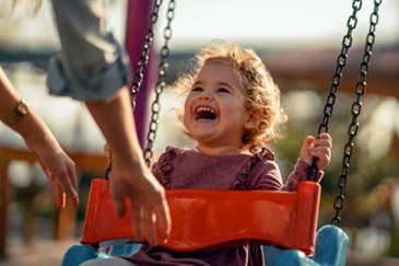 Child laughing on a playground swing while an adult pushes them
