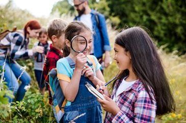 Children using magnifying glasses outdoors in a grassy field, examining plants together