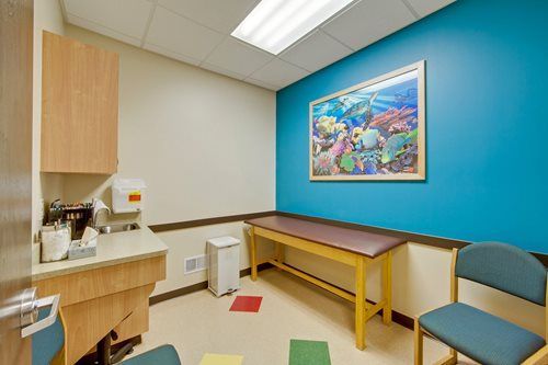 Small exam room with sink, counter, exam table, blue wall, and a framed picture.