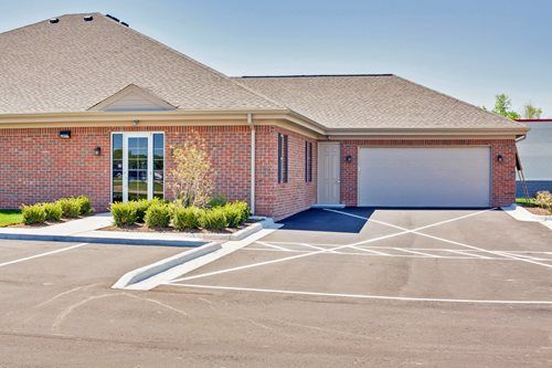 Brick office building with a sloped roof, glass entrance, garage door, and marked parking lot