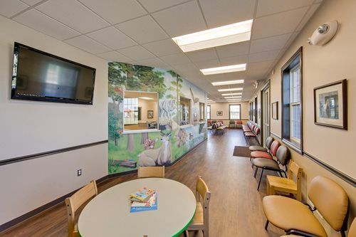 Bright medical waiting room with chairs, round table, wall art, and hallway mural.
