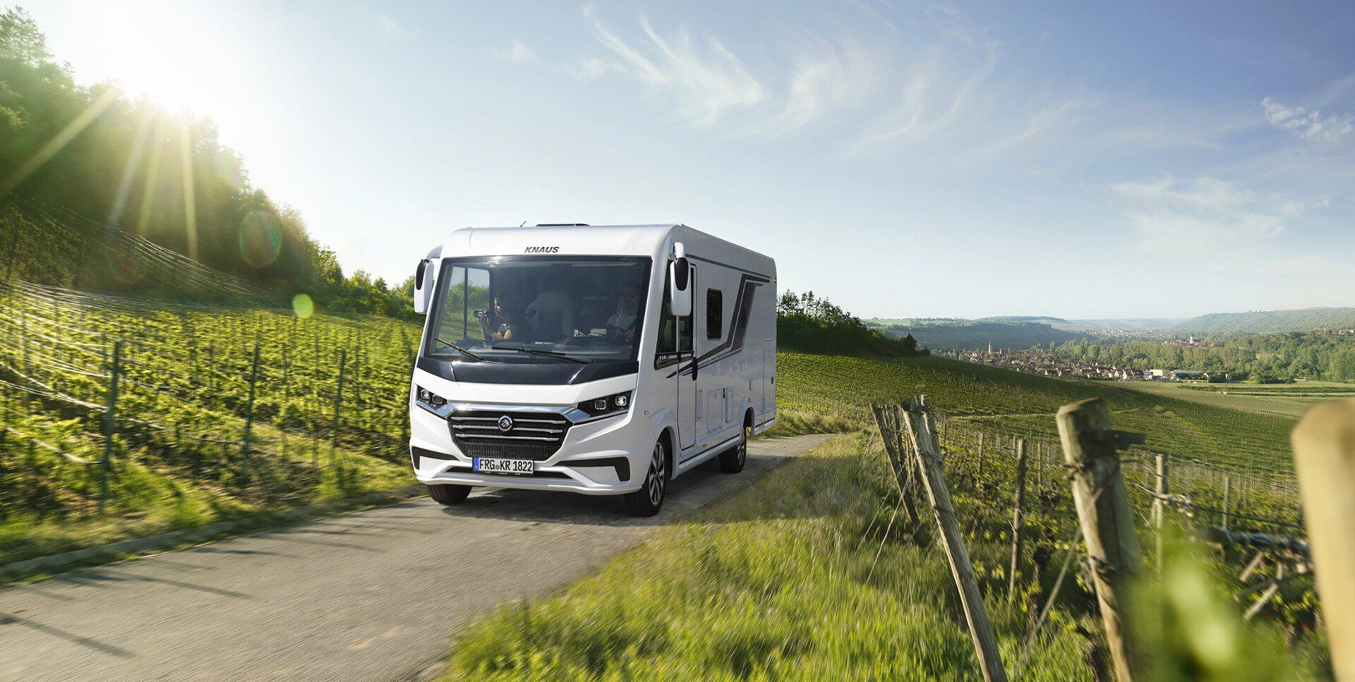 White RV on a road in a vineyard on a sunny day.
