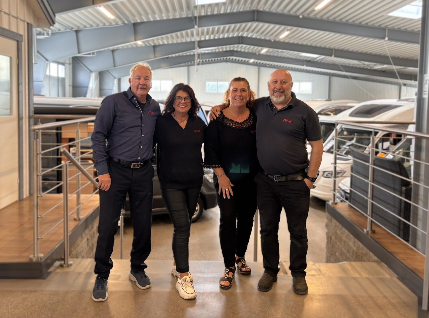 Four people standing together in a metal-roofed indoor barn or stable walkway