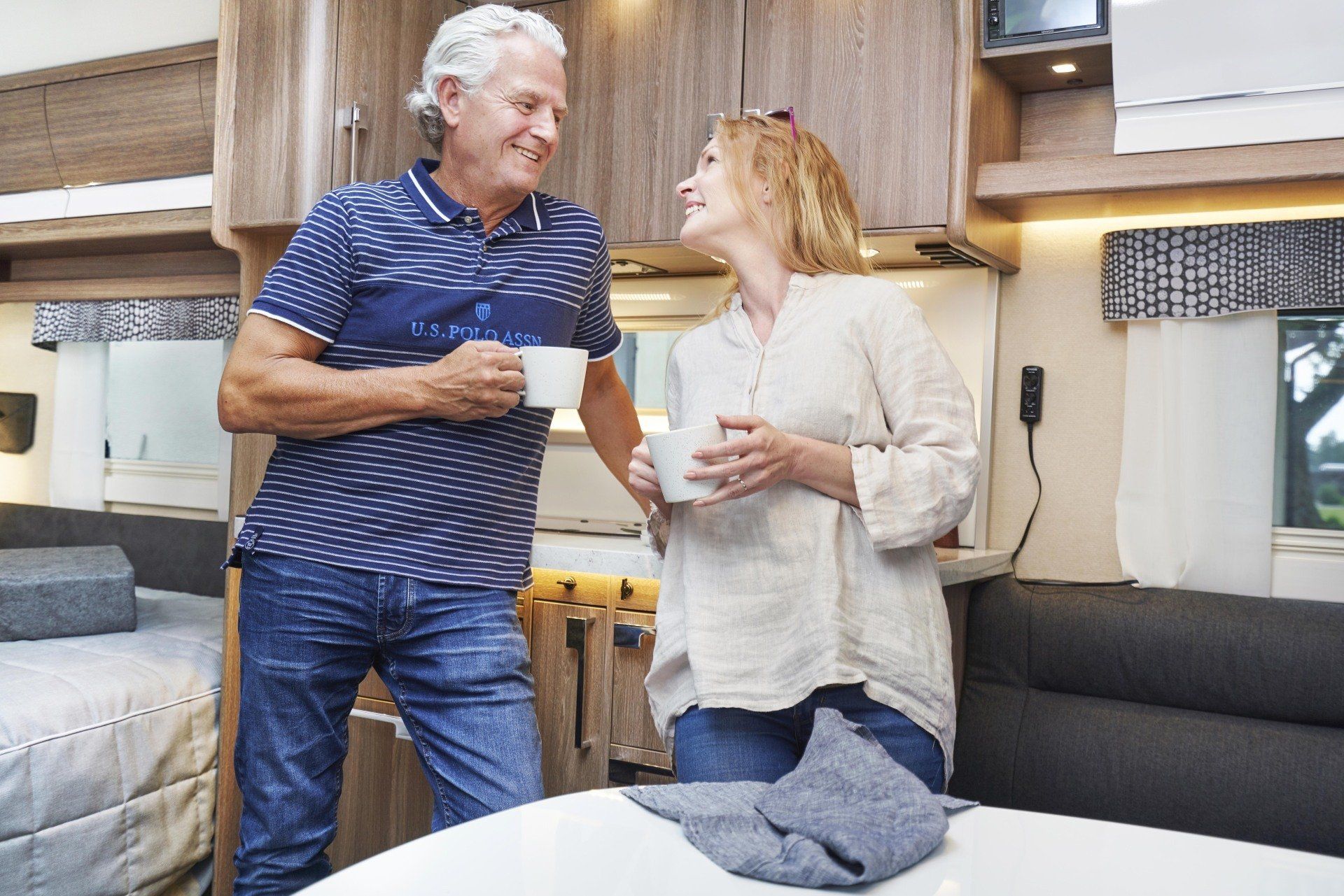 Couple smiling and holding mugs in a caravan interior.