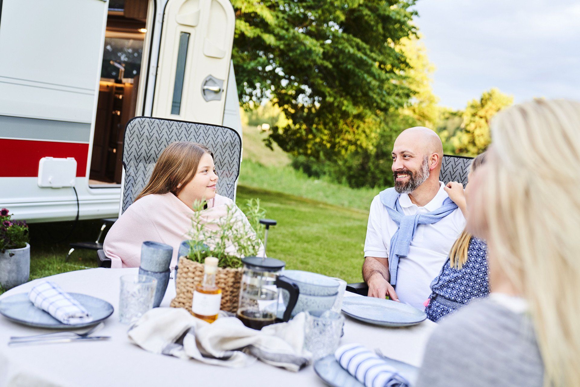 Family seated at a table outside a camper, smiling and talking.