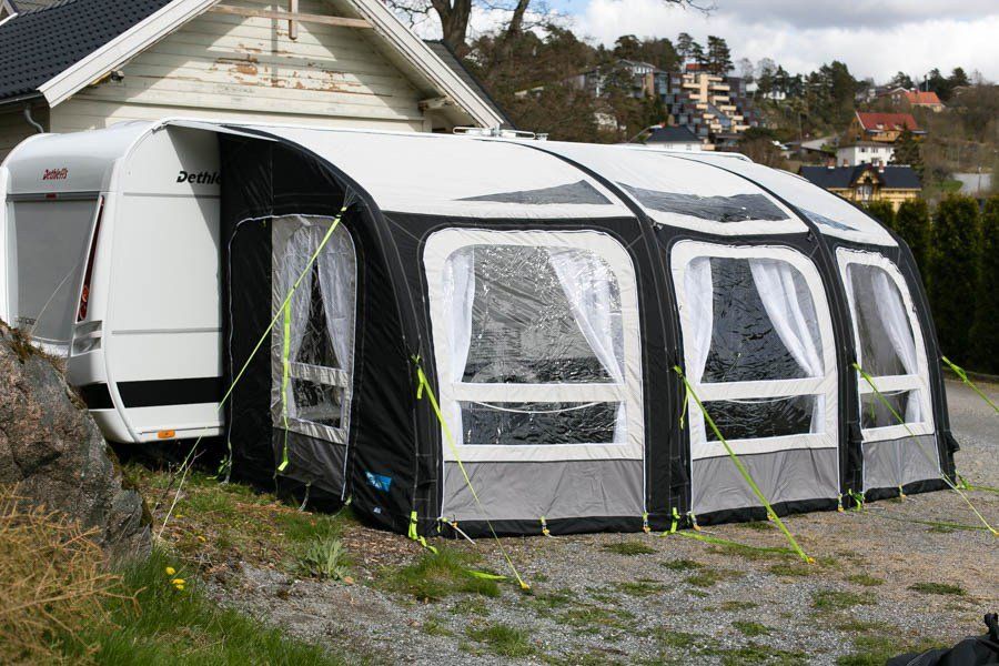 A white camper trailer with a large black and white inflatable awning set up on grass.