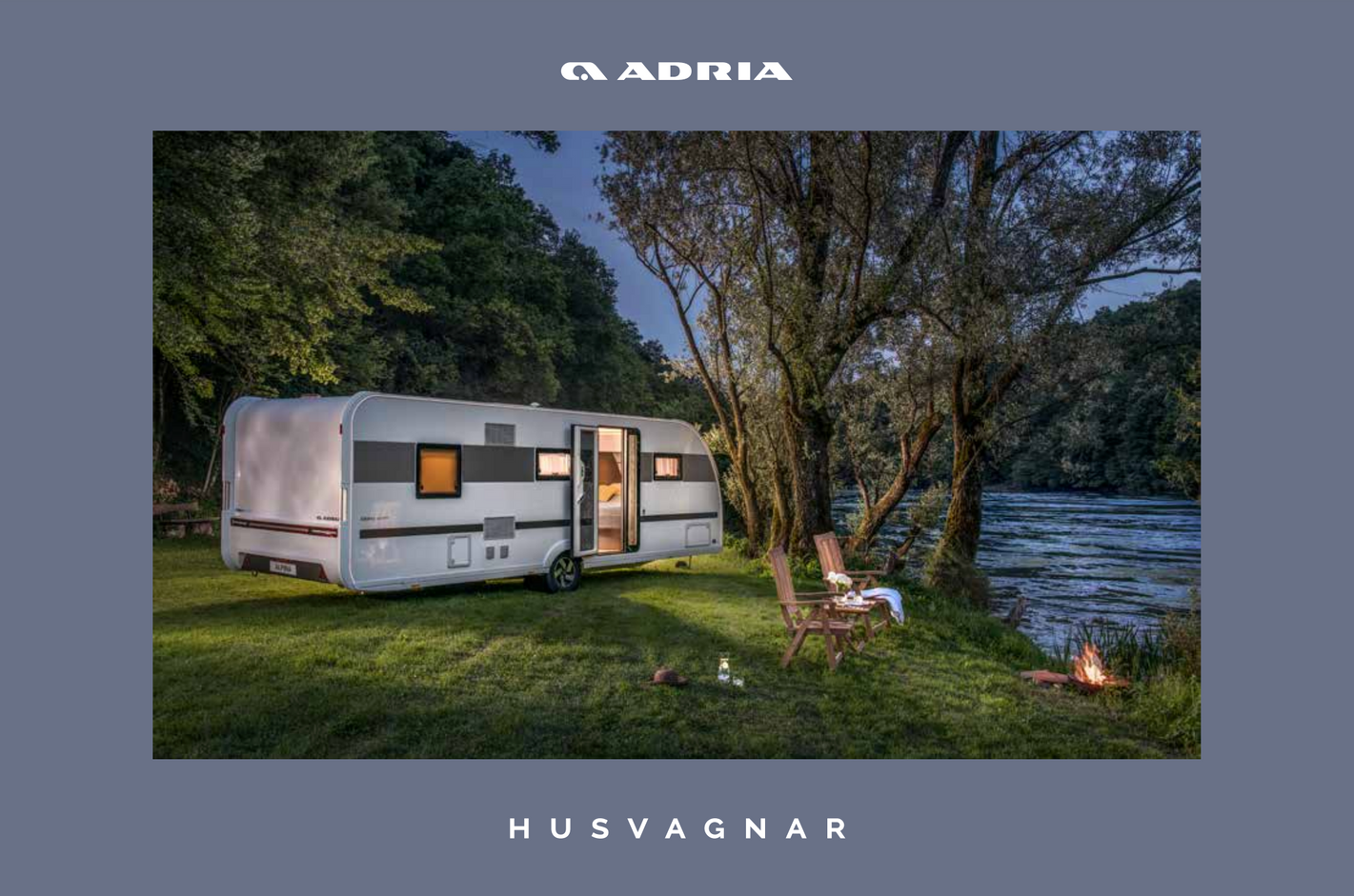 Caravan parked next to a river at dusk. The Adria Husvagnar trailer has lights on.