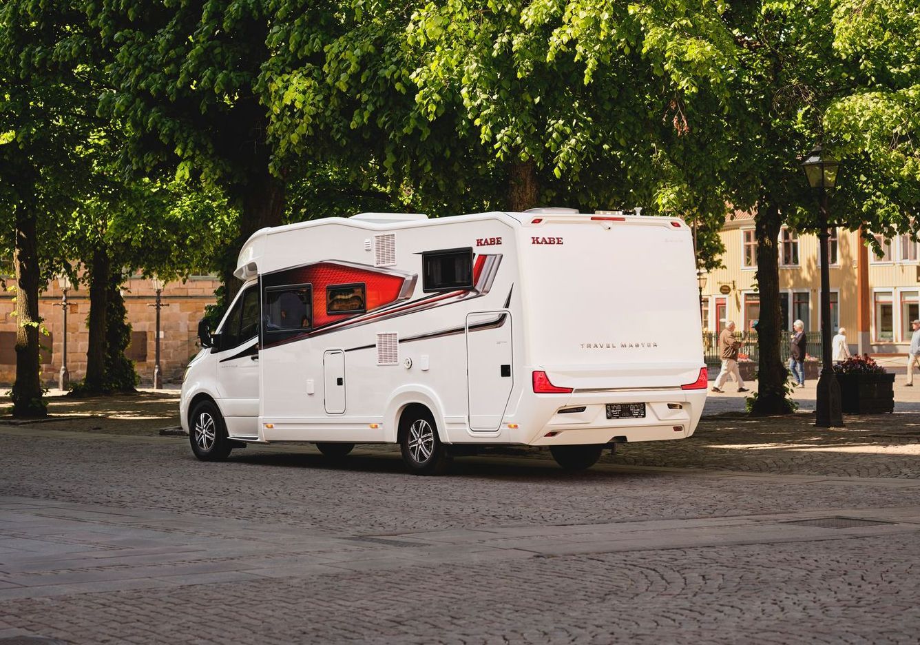 White campervan parked on cobblestone, red accents, trees in background.
