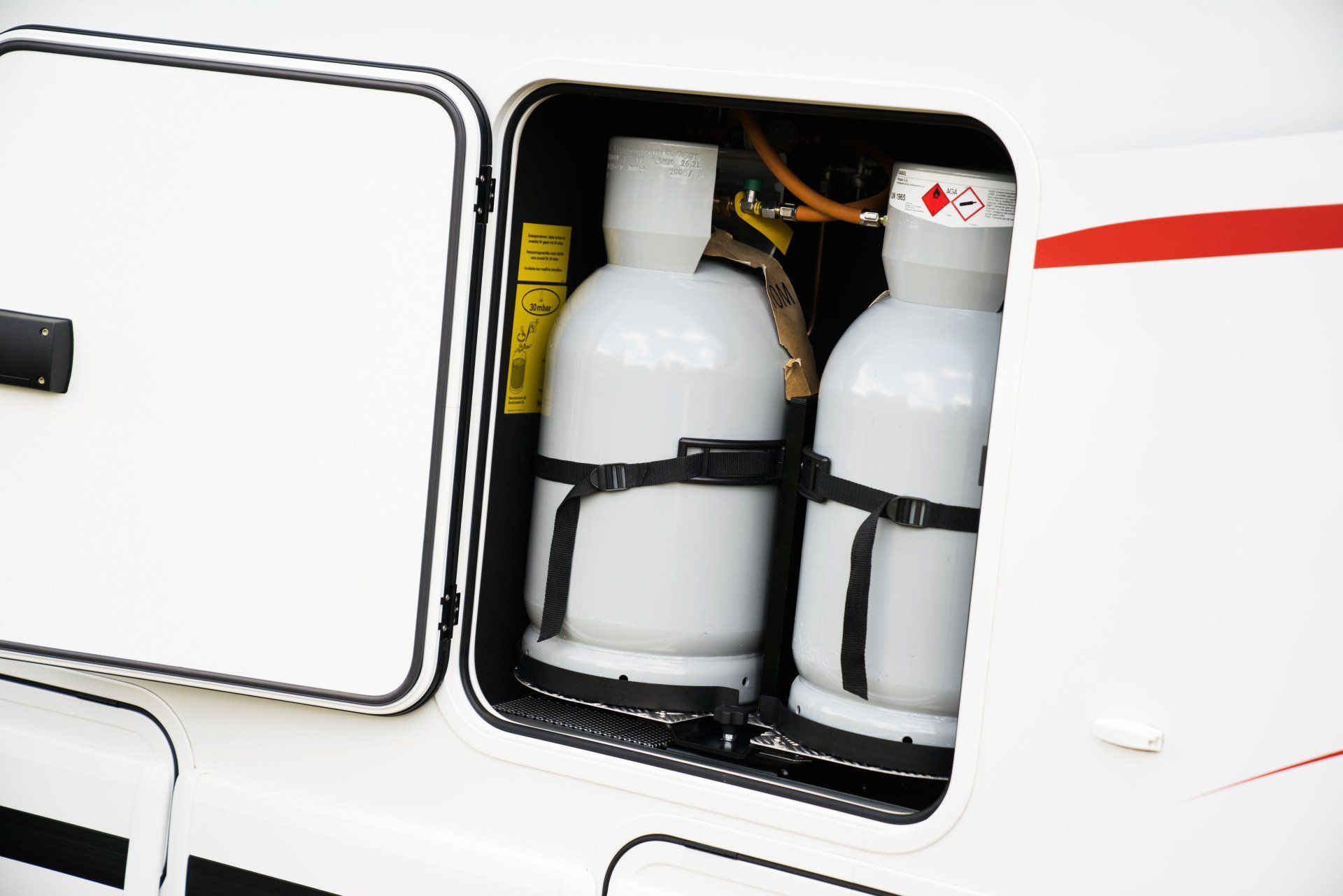 Two white propane tanks secured in a compartment of a recreational vehicle.